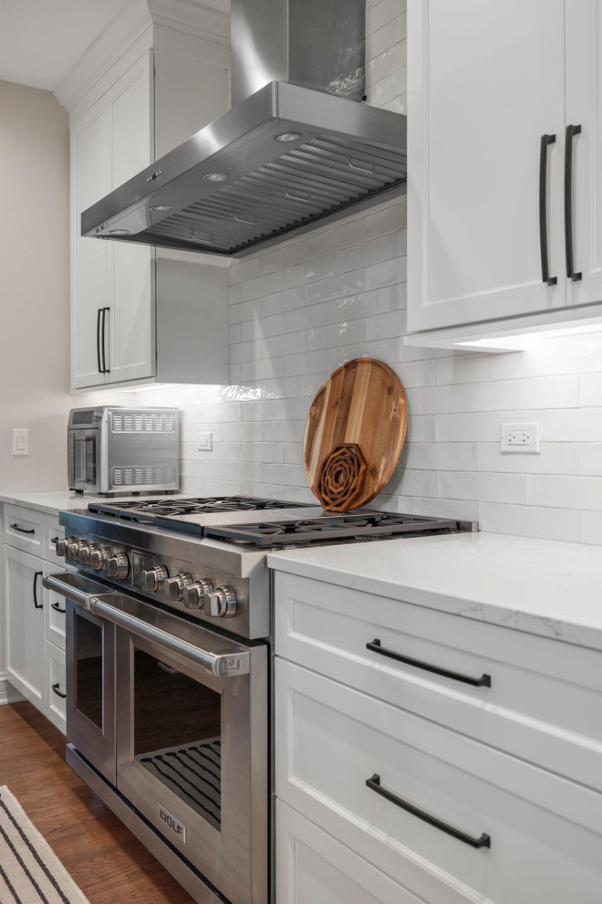 Example of a mid-sized transitional medium tone wood floor kitchen design in Chicago with shaker cabinets, quartz countertops, white backsplash, ceramic backsplash, stainless steel appliances, white countertops and white cabinets