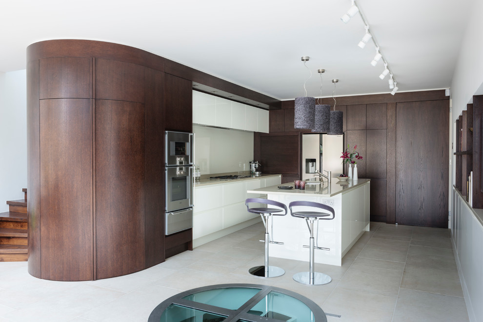 Photo of a contemporary kitchen in London with flat-panel cabinets, dark wood cabinets, white splashback, stainless steel appliances and glass sheet splashback.