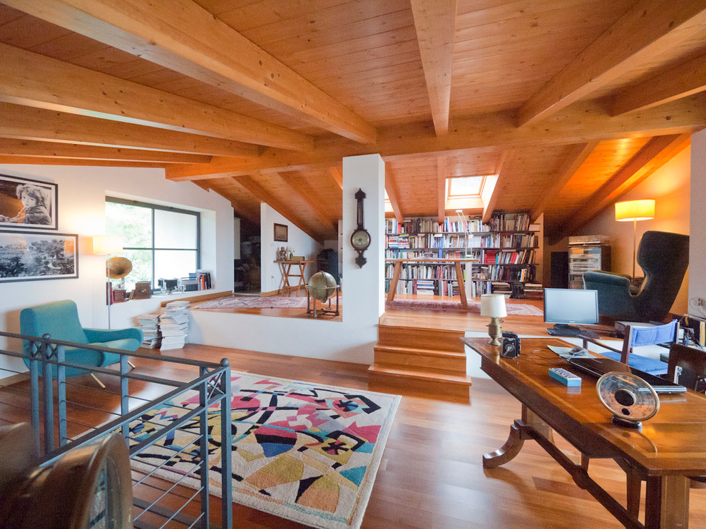 This is an example of a large country loft-style living room in Milan with a library, white walls, medium hardwood floors and no tv.