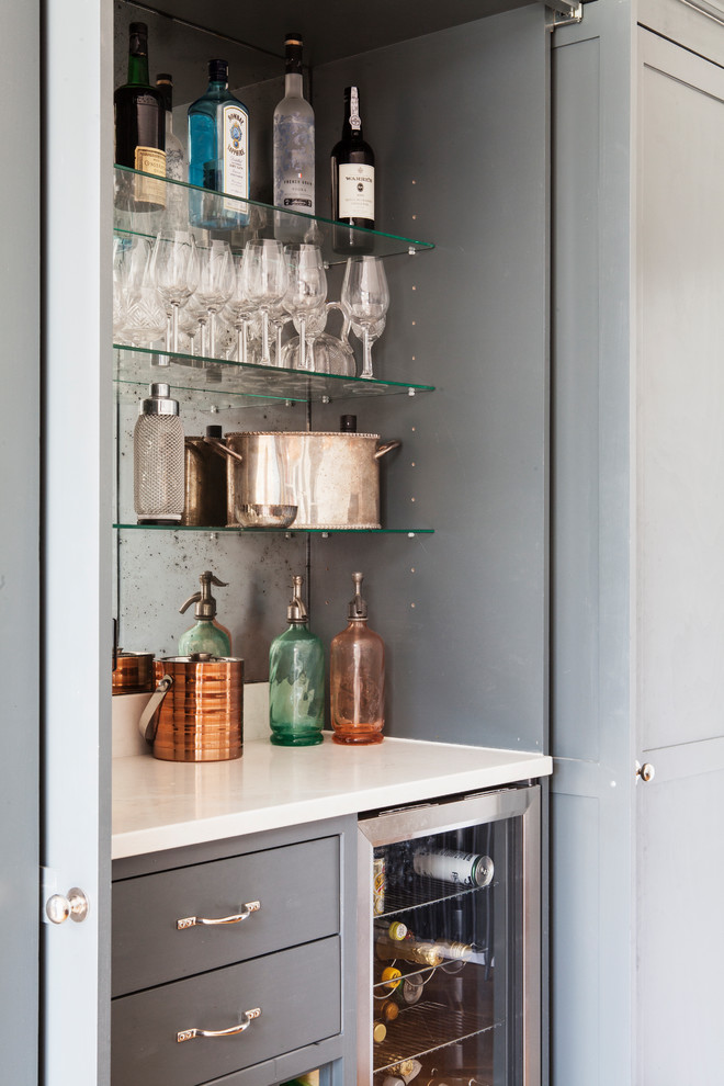 Modelo de bar en casa lineal clásico renovado pequeño sin pila con puertas de armario grises, salpicadero con efecto espejo y encimeras blancas