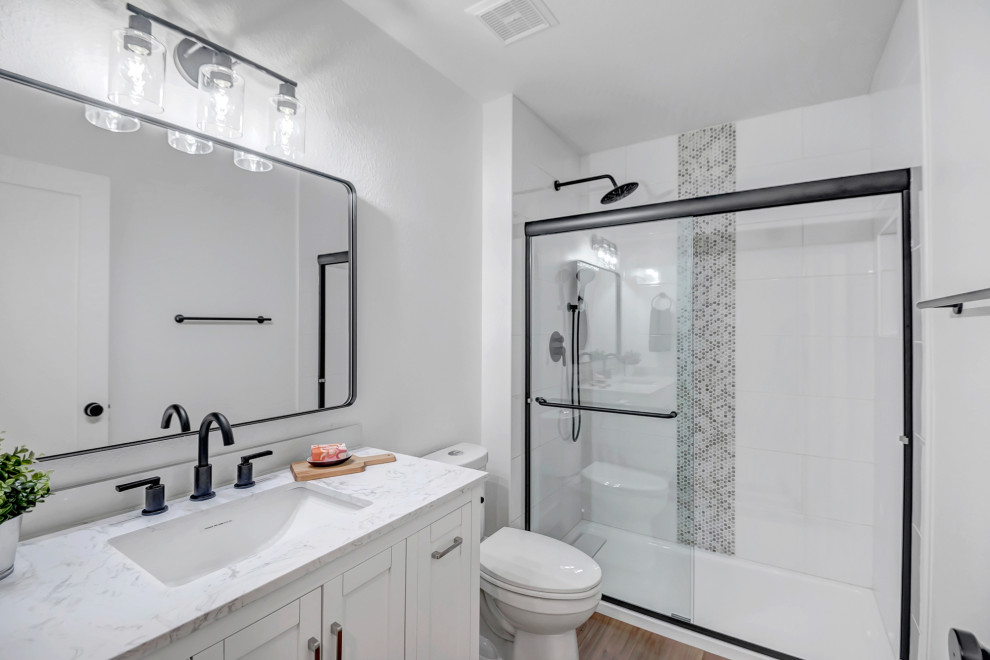 Idéer för mellanstora funkis grått badrum med dusch, med luckor med infälld panel, vita skåp, en toalettstol med hel cisternkåpa, glasskiva, vinylgolv, ett undermonterad handfat, marmorbänkskiva, brunt golv och dusch med skjutdörr