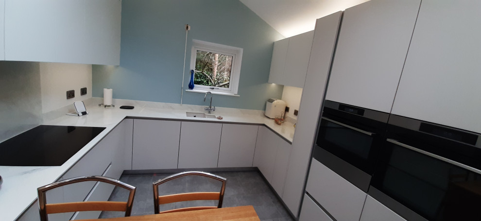Large modern u-shaped eat-in kitchen in Other with an undermount sink, flat-panel cabinets, white cabinets, onyx benchtops, white splashback, black appliances, linoleum floors, with island, grey floor and white benchtop.
