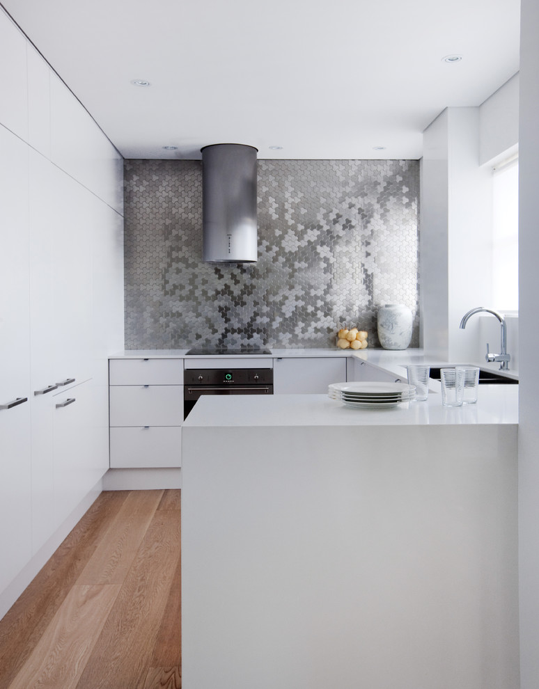This is an example of a small contemporary u-shaped eat-in kitchen in Sydney with metal splashback, black appliances, a drop-in sink, flat-panel cabinets, white cabinets, quartz benchtops and medium hardwood floors.