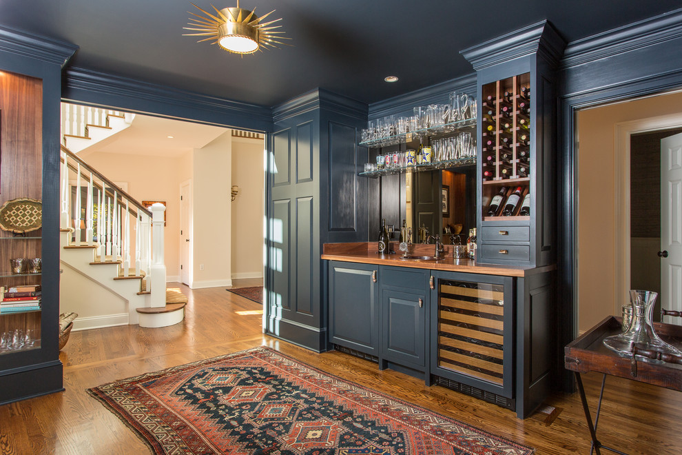 This is an example of a traditional single-wall wet bar in New York with a drop-in sink, raised-panel cabinets, blue cabinets, wood benchtops, dark hardwood floors and brown benchtop.
