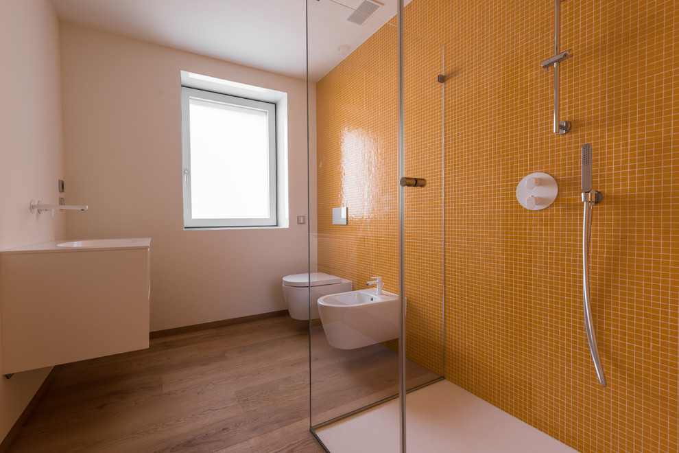 Design ideas for a mid-sized contemporary 3/4 bathroom in Other with flat-panel cabinets, white cabinets, a curbless shower, a wall-mount toilet, orange tile, glass tile, white walls, light hardwood floors, an integrated sink, brown floor and a hinged shower door.
