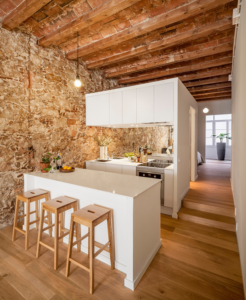 This is an example of a mid-sized contemporary galley open plan kitchen in Barcelona with flat-panel cabinets, white cabinets, a peninsula, an undermount sink, mirror splashback, stainless steel appliances, medium hardwood floors and brown floor.