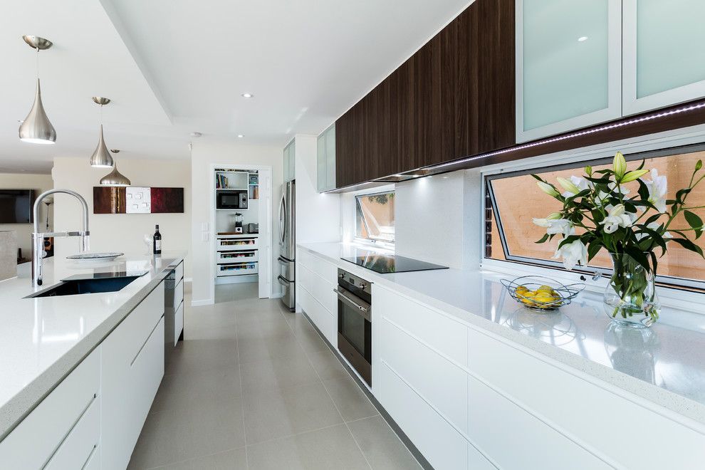 This is an example of a large contemporary galley kitchen in Gold Coast - Tweed with flat-panel cabinets, quartz benchtops, stainless steel appliances, porcelain floors, with island, an undermount sink and white cabinets.