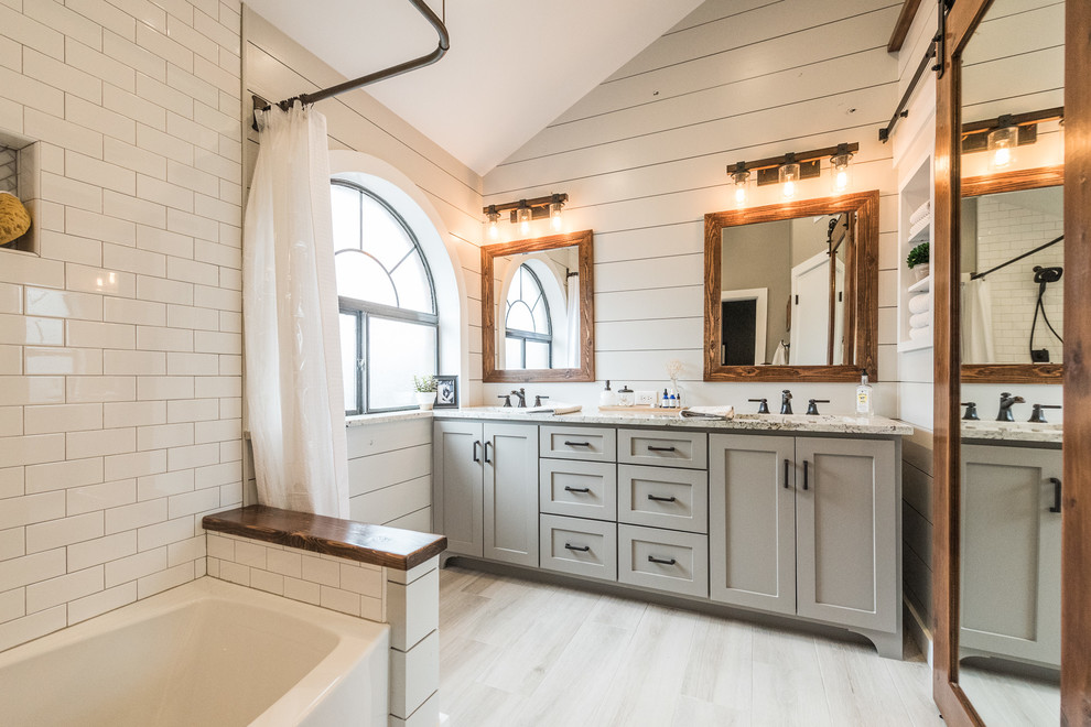 This is an example of a mid-sized country master bathroom in Dallas with shaker cabinets, grey cabinets, an alcove tub, a shower/bathtub combo, a one-piece toilet, gray tile, porcelain tile, grey walls, porcelain floors, an undermount sink and granite benchtops.