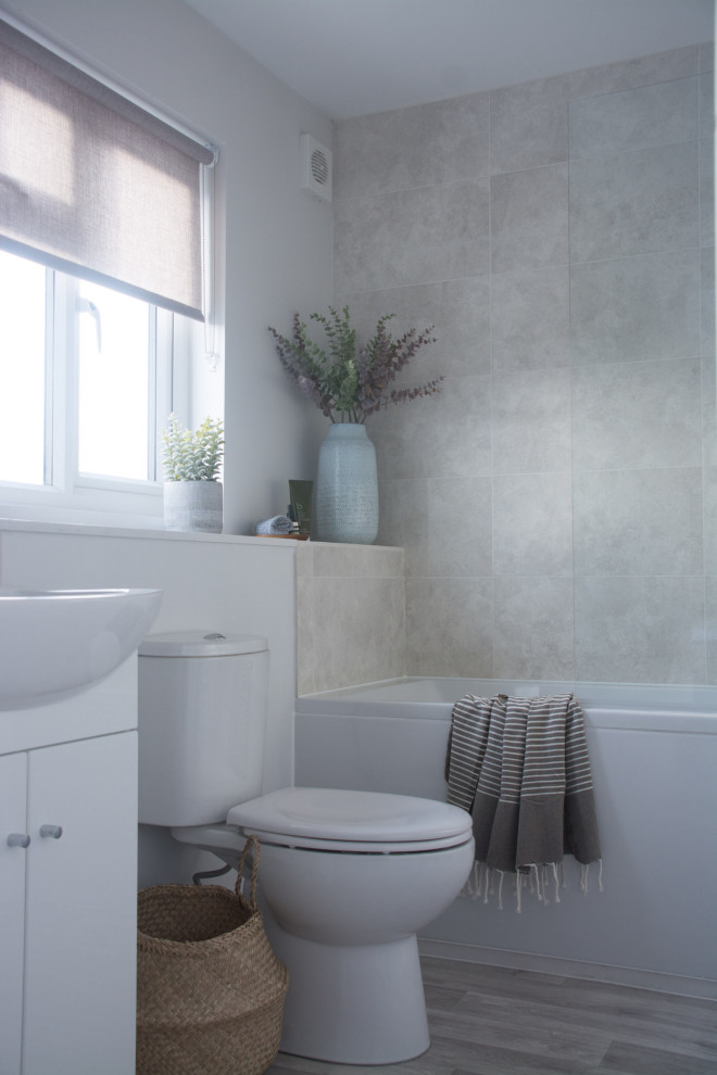 This is an example of a small modern master bathroom in Cambridgeshire with flat-panel cabinets, white cabinets, a drop-in tub, a shower/bathtub combo, a one-piece toilet, gray tile, porcelain tile, grey walls, laminate floors, a drop-in sink, laminate benchtops, brown floor, a hinged shower door, white benchtops, a single vanity and a built-in vanity.
