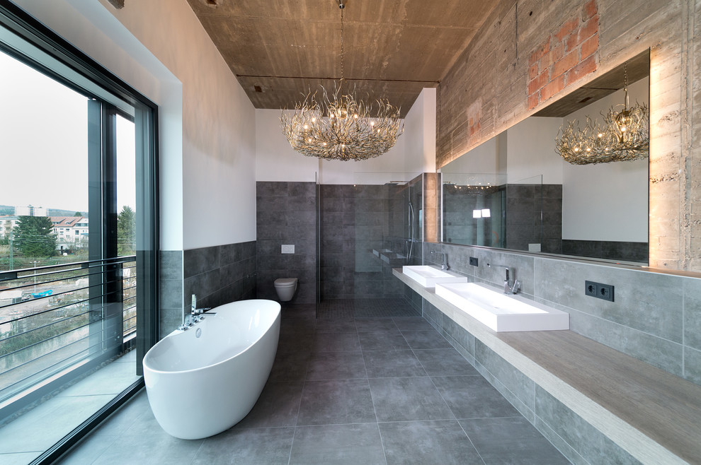 Large industrial master bathroom in Other with a freestanding tub, a curbless shower, stone tile, ceramic floors, a vessel sink, solid surface benchtops, grey floor, an open shower, a wall-mount toilet, gray tile and white walls.
