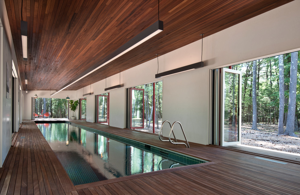 Large country indoor rectangular lap pool in New York with a pool house and decking.