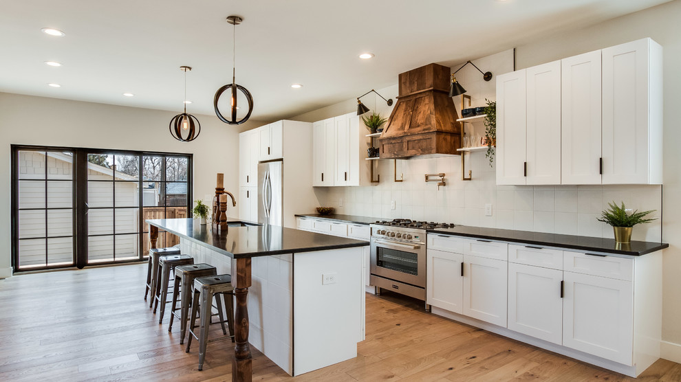 Example of a mid-sized farmhouse galley beige floor and light wood floor eat-in kitchen design in Denver with an undermount sink, shaker cabinets, white cabinets, white backsplash, stainless steel appliances, an island, black countertops and ceramic backsplash