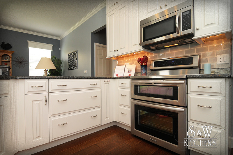 Open concept kitchen - mid-sized transitional u-shaped dark wood floor open concept kitchen idea in Orlando with a double-bowl sink, raised-panel cabinets, white cabinets, granite countertops, beige backsplash, subway tile backsplash and stainless steel appliances