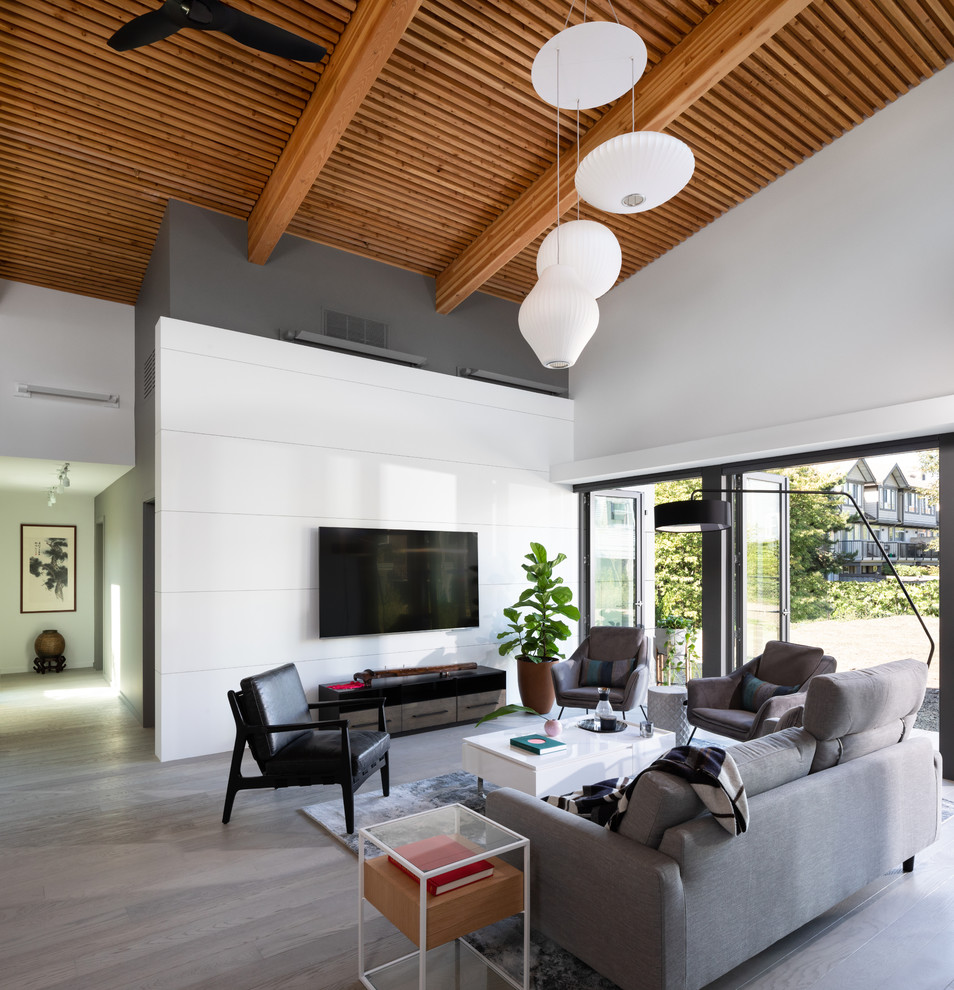 Photo of a contemporary open concept living room in Vancouver with white walls, light hardwood floors, a wall-mounted tv and beige floor.