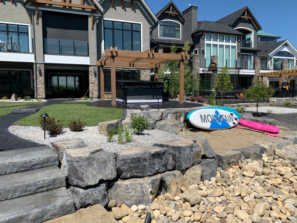 Inspiration for a large beach style backyard xeriscape in Calgary with a retaining wall and river rock.
