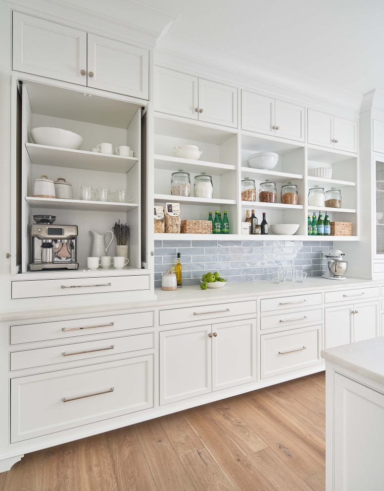 This is an example of a kitchen pantry in Charlotte with a farmhouse sink, beaded inset cabinets, white cabinets, marble benchtops, white splashback, marble splashback, stainless steel appliances, medium hardwood floors, multiple islands, brown floor, white benchtop and timber.