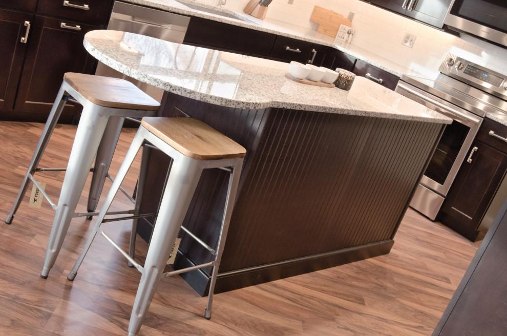 L-shaped kitchen photo with a single-bowl sink, shaker cabinets, dark wood cabinets, granite countertops, white backsplash, stainless steel appliances and an island