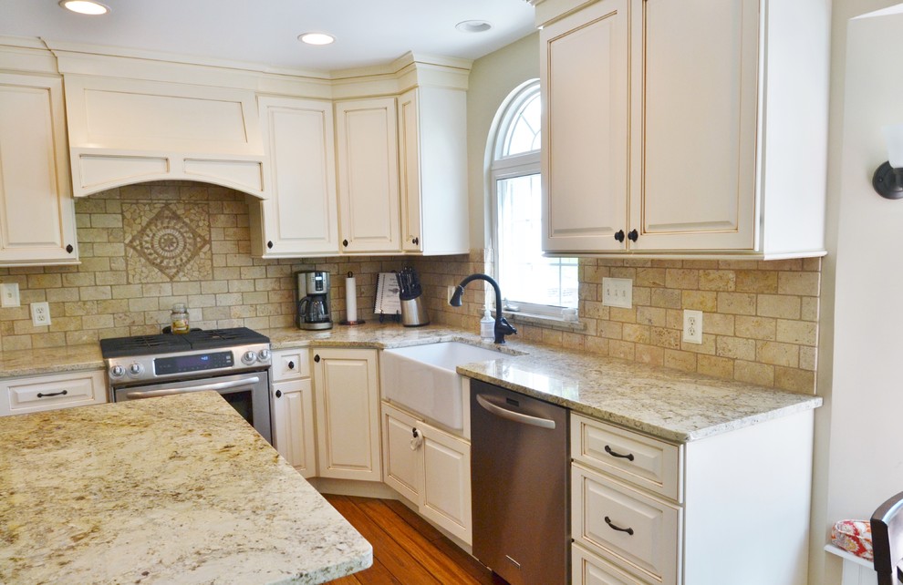 Mid-sized traditional l-shaped kitchen in St Louis with a farmhouse sink, raised-panel cabinets, beige cabinets, granite benchtops, beige splashback, stone tile splashback, stainless steel appliances, bamboo floors and with island.
