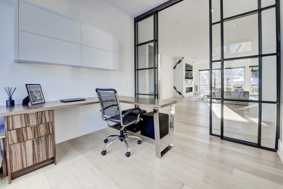 Imagen de despacho actual de tamaño medio con biblioteca, paredes blancas, suelo de madera clara, escritorio independiente y suelo beige