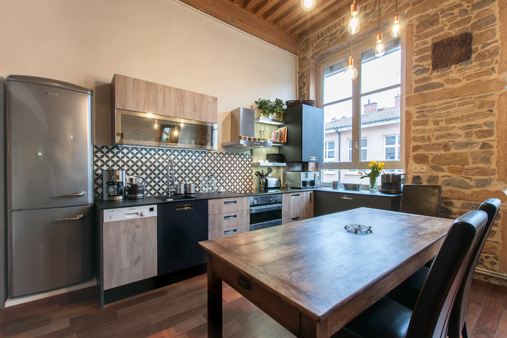 Photo of a mid-sized industrial l-shaped eat-in kitchen in Lyon with light wood cabinets, solid surface benchtops, cement tile splashback and stainless steel appliances.