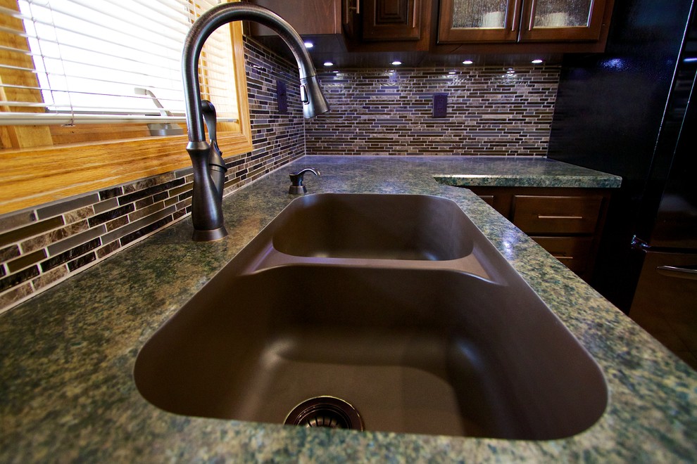 Example of a mid-sized u-shaped kitchen design with an undermount sink, dark wood cabinets, laminate countertops, multicolored backsplash, glass tile backsplash, black appliances and an island