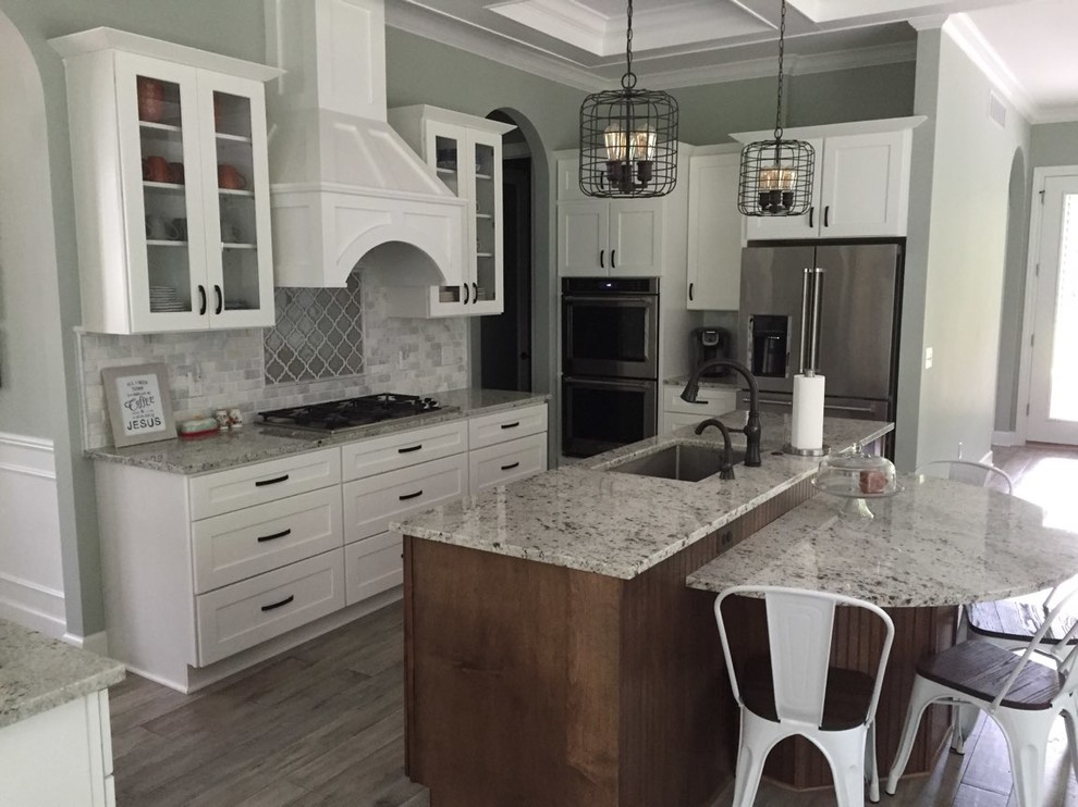 Photo of a mid-sized transitional galley eat-in kitchen in Detroit with a single-bowl sink, recessed-panel cabinets, white cabinets, granite benchtops, multi-coloured splashback, ceramic splashback, stainless steel appliances, plywood floors, with island and grey floor.