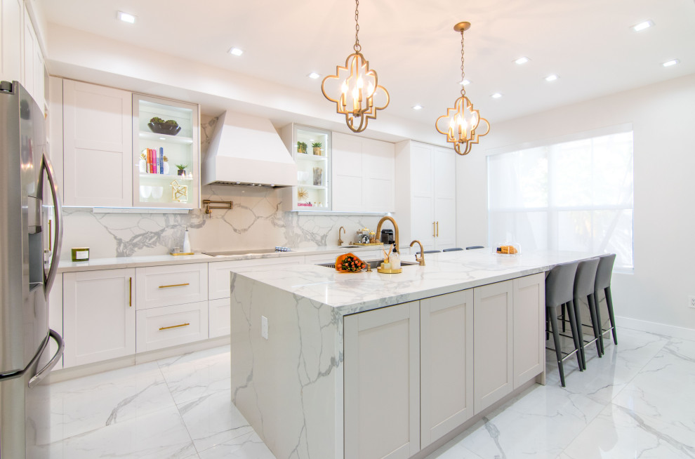 Example of a large transitional l-shaped porcelain tile and white floor open concept kitchen design in Miami with an undermount sink, shaker cabinets, white cabinets, quartz countertops, white backsplash, porcelain backsplash, stainless steel appliances, an island and white countertops
