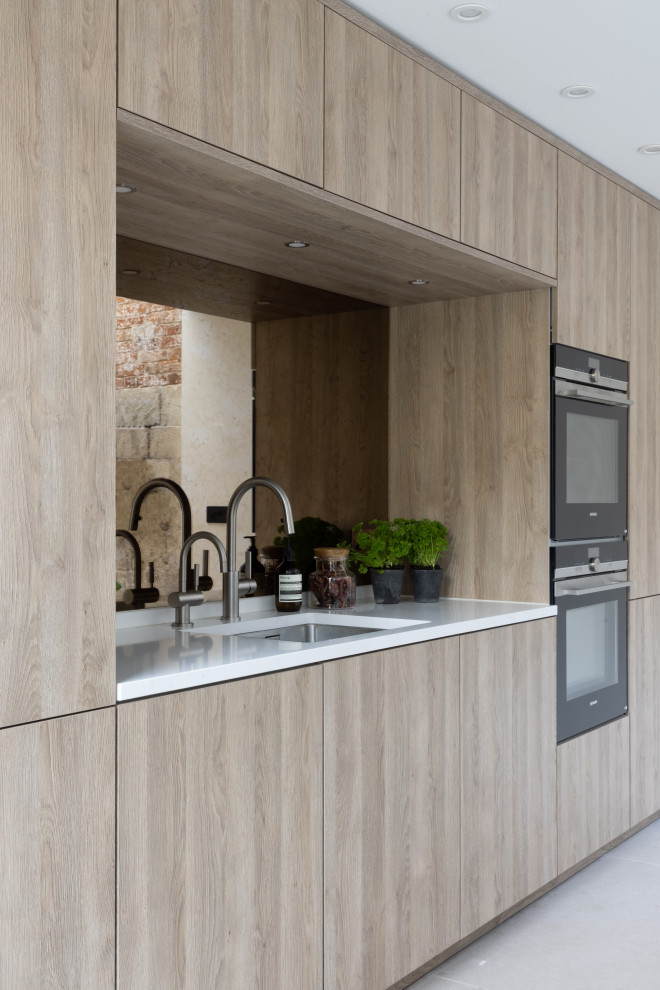 Medium sized scandi kitchen/diner in Hampshire with flat-panel cabinets, medium wood cabinets, composite countertops, mirror splashback, black appliances, an island and white worktops.