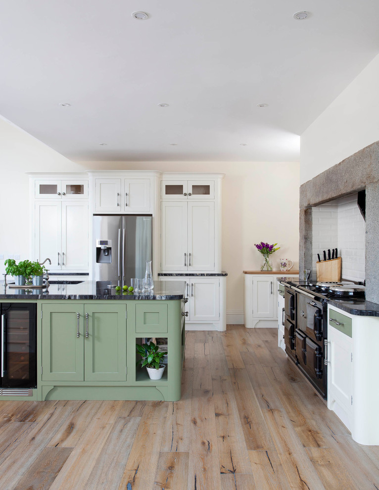 Inspiration for a large country l-shaped eat-in kitchen in Belfast with an undermount sink, shaker cabinets, green cabinets, granite benchtops, white splashback, ceramic splashback, stainless steel appliances, light hardwood floors, with island and brown floor.