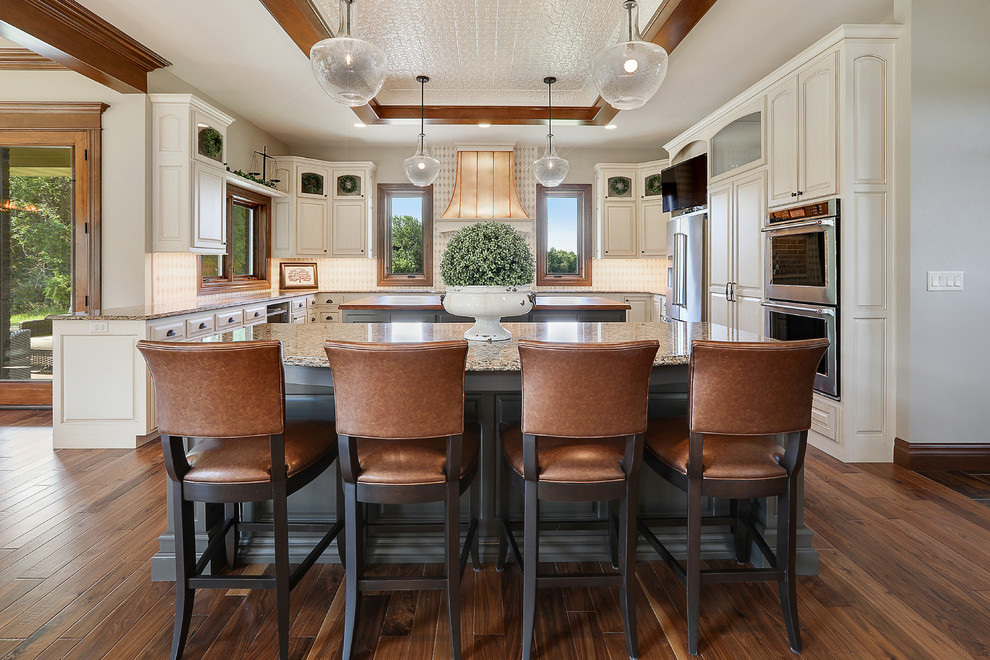 This is an example of a traditional u-shaped kitchen in Other with raised-panel cabinets, white cabinets, beige splashback, stainless steel appliances, dark hardwood floors, multiple islands and brown floor.