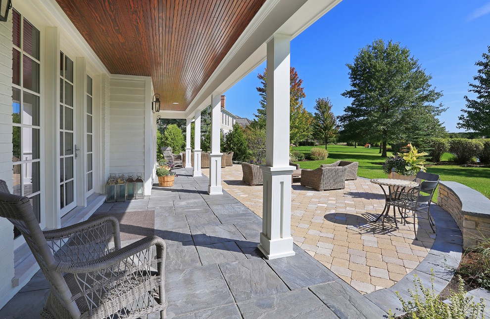 Design ideas for a large traditional backyard patio in Chicago with natural stone pavers and a roof extension.