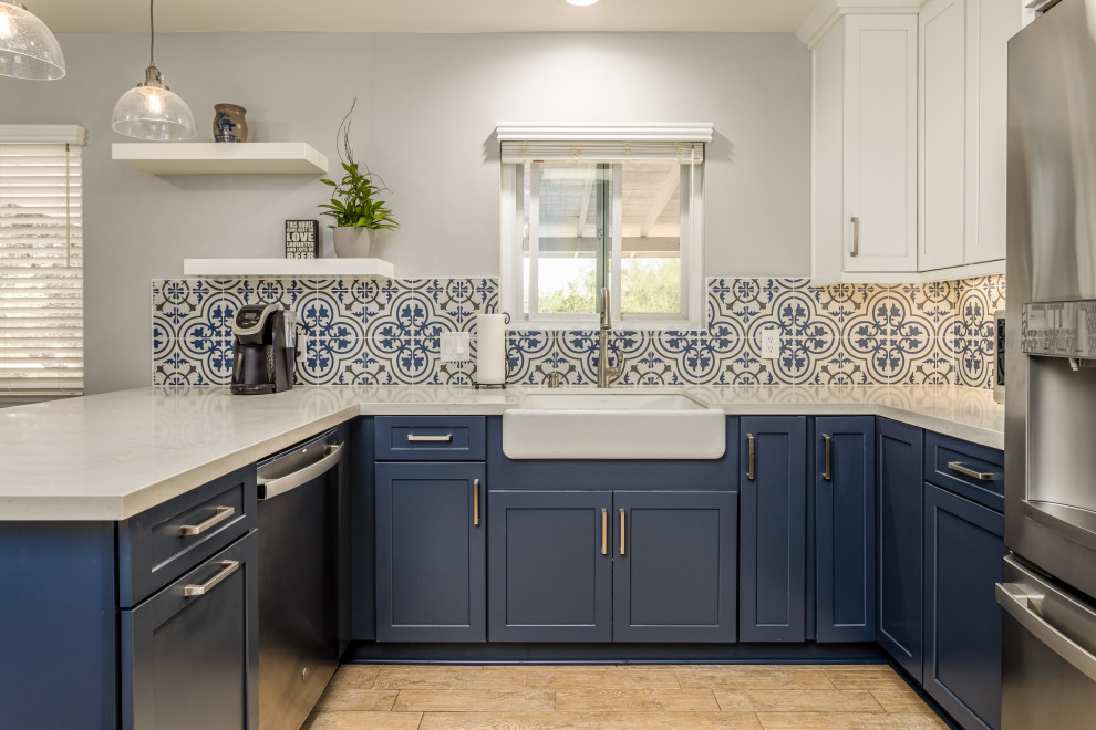 This is an example of a mid-sized beach style l-shaped kitchen in San Diego with a farmhouse sink, shaker cabinets, blue cabinets, quartz benchtops, blue splashback, porcelain splashback, stainless steel appliances, light hardwood floors and white benchtop.