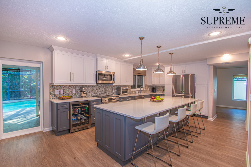 Large trendy u-shaped vinyl floor, brown floor and coffered ceiling eat-in kitchen photo in Tampa with an undermount sink, shaker cabinets, gray cabinets, quartz countertops, multicolored backsplash, glass tile backsplash, stainless steel appliances, an island and white countertops