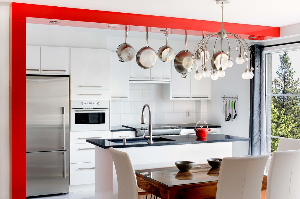 This is an example of a contemporary galley eat-in kitchen in Montreal with an undermount sink, flat-panel cabinets, white cabinets, quartz benchtops, white splashback and stainless steel appliances.