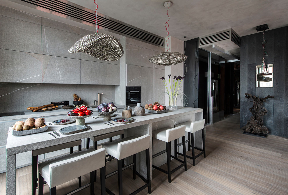 Inspiration for a mid-sized galley open plan kitchen in Moscow with an integrated sink, flat-panel cabinets, grey cabinets, grey splashback, with island, beige floor, limestone benchtops, limestone splashback, stainless steel appliances and light hardwood floors.