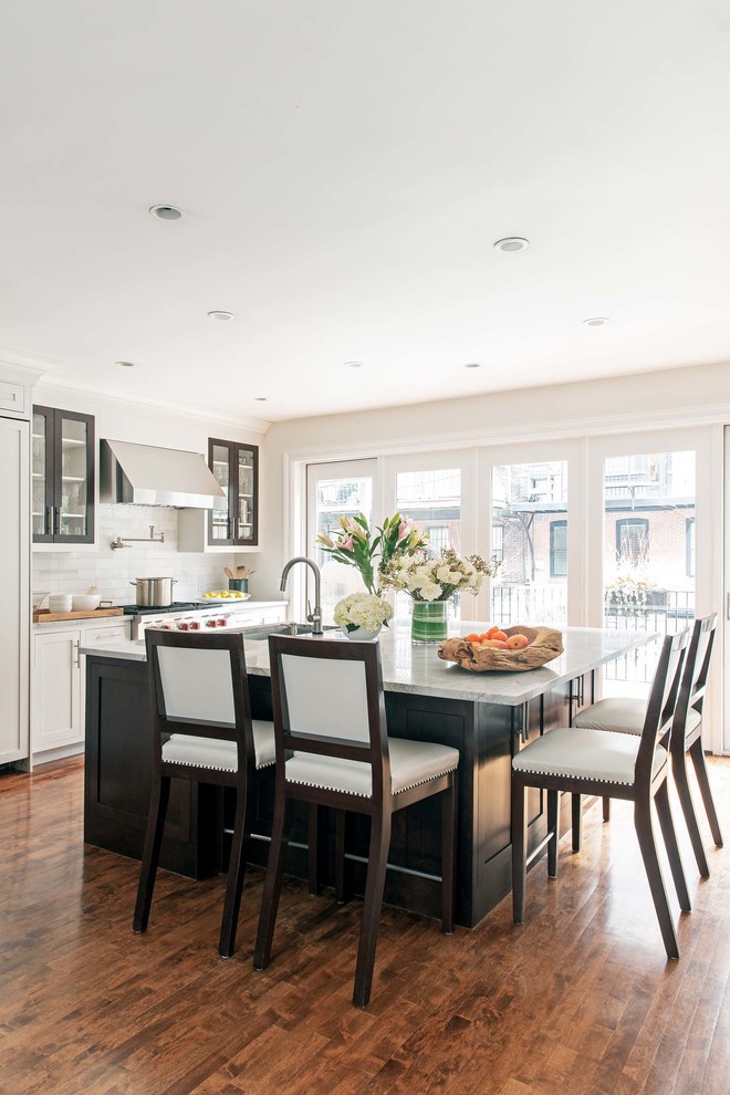 This is an example of a mid-sized transitional single-wall eat-in kitchen in Boston with glass-front cabinets, grey splashback, stainless steel appliances, medium hardwood floors, with island, grey benchtop, white cabinets, an undermount sink and ceramic splashback.