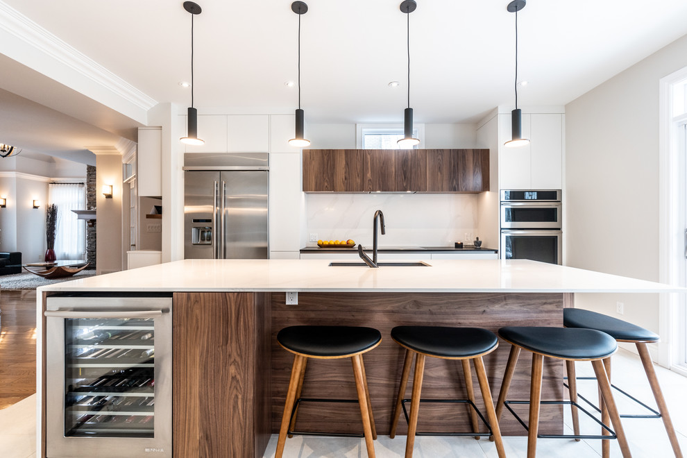 This is an example of a contemporary single-wall kitchen in Montreal with an undermount sink, flat-panel cabinets, white cabinets, white splashback, stainless steel appliances, with island, white floor and white benchtop.