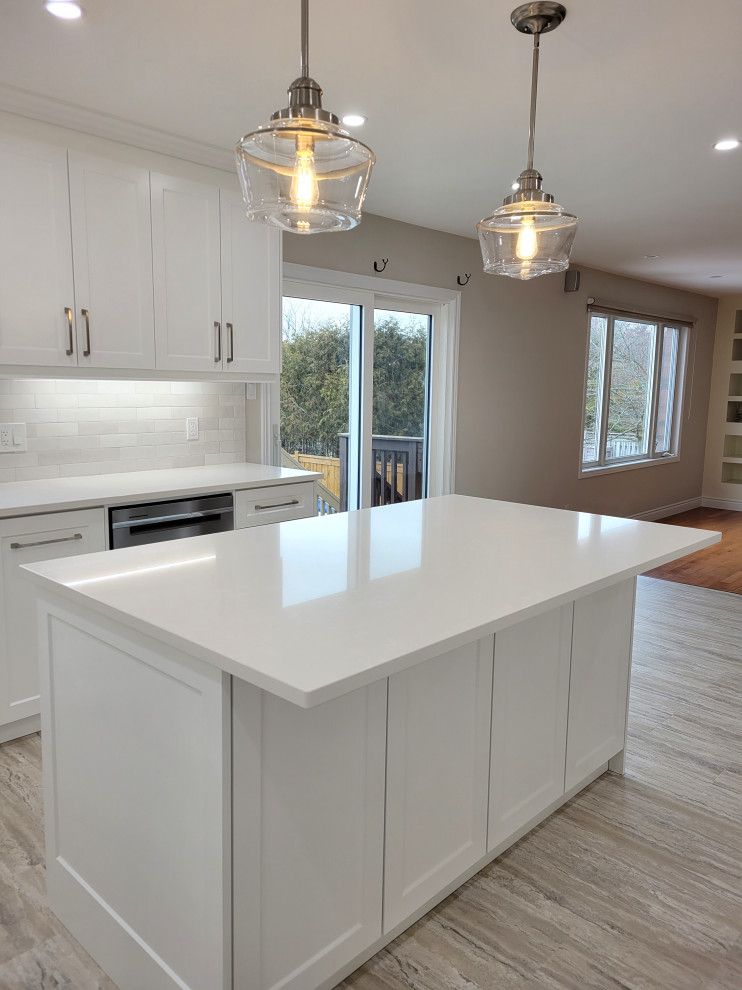 Huge transitional u-shaped vinyl floor and multicolored floor eat-in kitchen photo with an undermount sink, white cabinets, quartzite countertops, gray backsplash, stone tile backsplash, white appliances, an island and white countertops