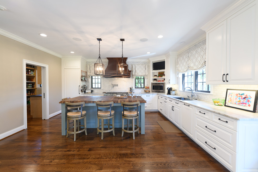 Example of a large transitional l-shaped dark wood floor and brown floor kitchen design with an undermount sink, raised-panel cabinets, white cabinets, quartzite countertops, white backsplash, marble backsplash, stainless steel appliances and an island