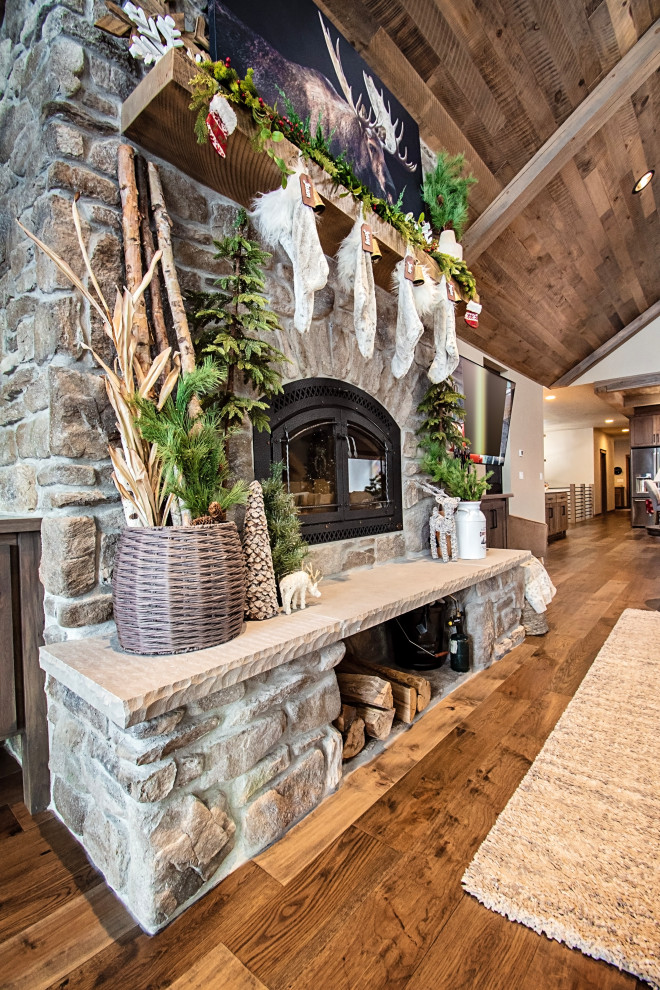 Inspiration for a large rustic open concept medium tone wood floor, multicolored floor and vaulted ceiling living room remodel with beige walls, a standard fireplace, a stacked stone fireplace and a wall-mounted tv