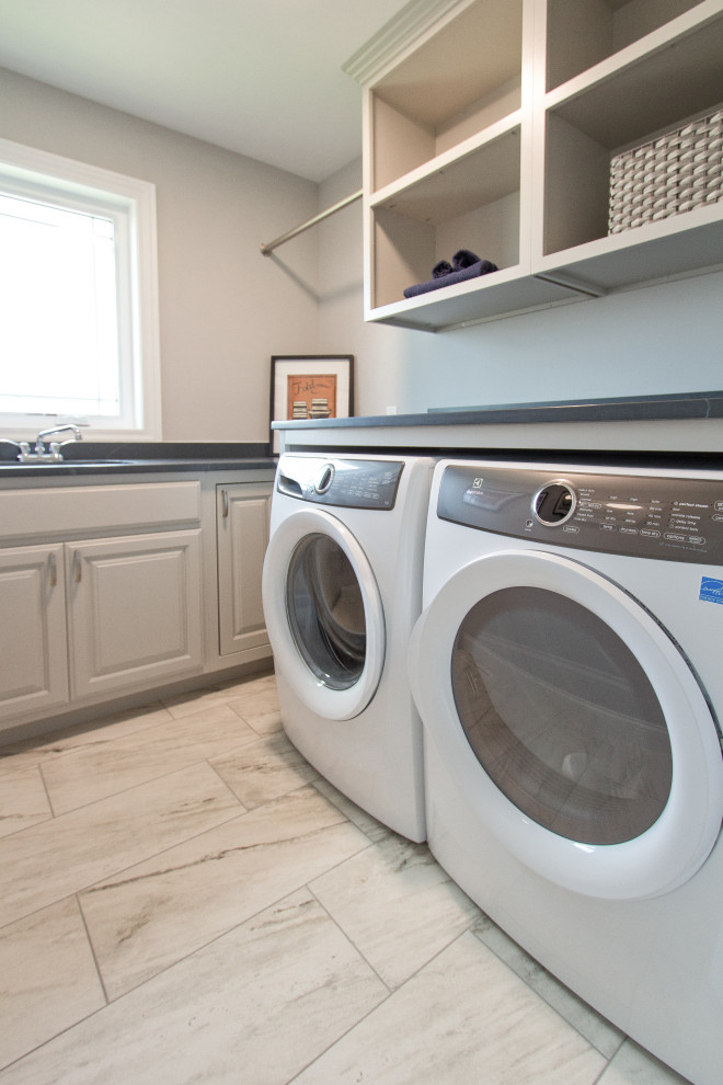 Klassische Waschküche mit Unterbauwaschbecken, profilierten Schrankfronten, Porzellan-Bodenfliesen, Waschmaschine und Trockner nebeneinander und schwarzer Arbeitsplatte in Sonstige