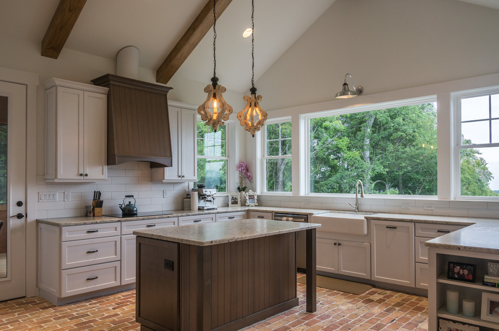 Example of a large mountain style u-shaped brick floor and brown floor open concept kitchen design with a farmhouse sink, shaker cabinets, white cabinets, granite countertops, white backsplash, ceramic backsplash, stainless steel appliances, an island and beige countertops