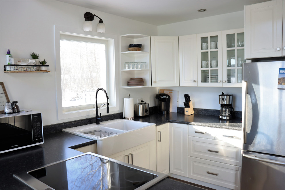 Photo of a small rustic u-shaped kitchen/diner in Other with a belfast sink, louvered cabinets, white cabinets, laminate countertops, stainless steel appliances, a breakfast bar and black worktops.