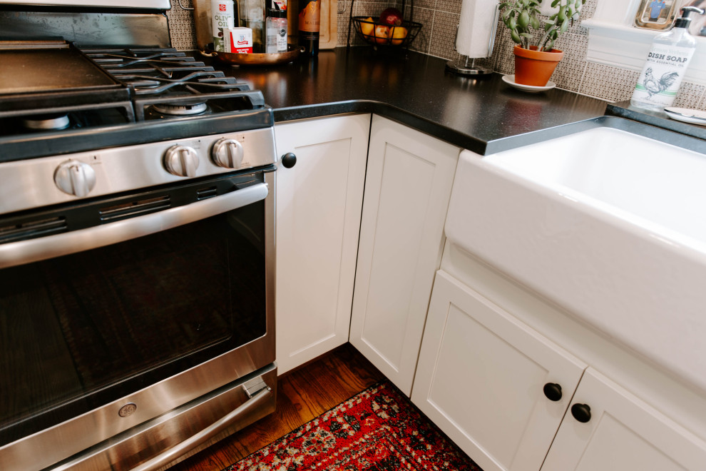 Inspiration for a mid-sized traditional u-shaped eat-in kitchen in DC Metro with a farmhouse sink, glass-front cabinets, white cabinets, quartz benchtops, grey splashback, ceramic splashback, stainless steel appliances and black benchtop.