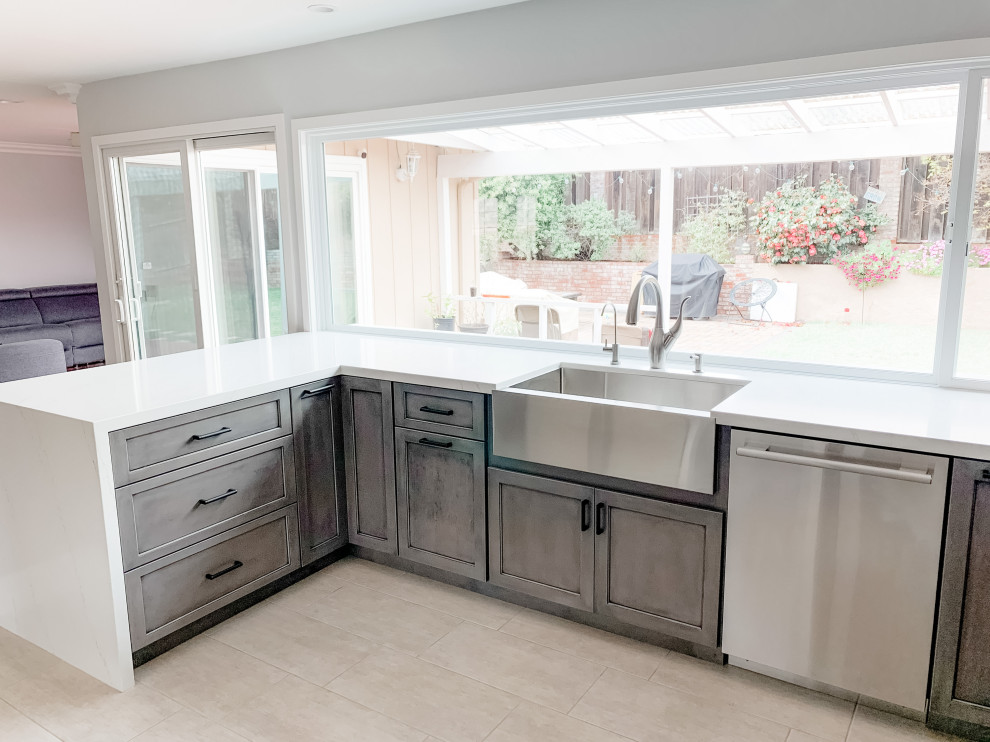This is an example of a medium sized contemporary u-shaped kitchen in San Francisco with a belfast sink, shaker cabinets, grey cabinets, engineered stone countertops, white splashback, engineered quartz splashback, stainless steel appliances, porcelain flooring, a breakfast bar, beige floors and white worktops.