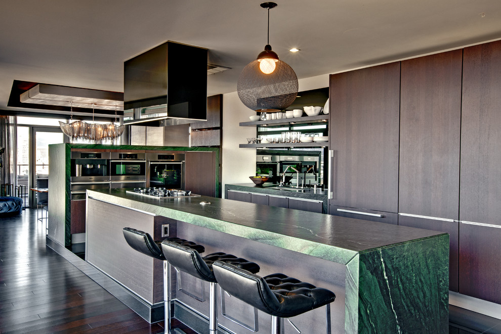Photo of a mid-sized contemporary u-shaped open plan kitchen in Los Angeles with a single-bowl sink, flat-panel cabinets, dark wood cabinets, soapstone benchtops, black splashback, glass sheet splashback, panelled appliances, marble floors, with island and brown floor.