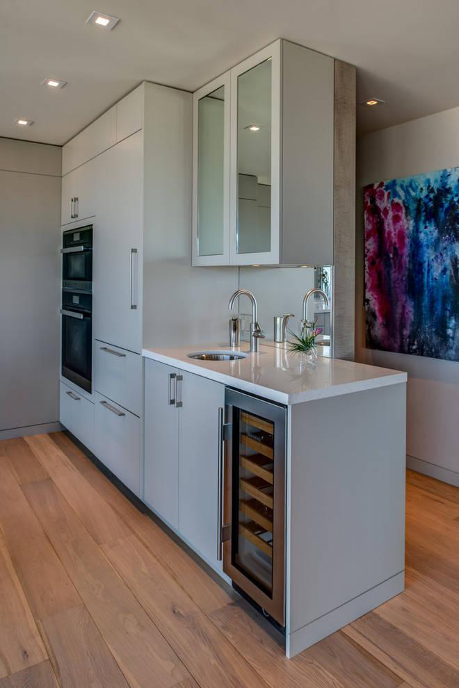 Design ideas for a small modern galley kitchen in San Francisco with a drop-in sink, flat-panel cabinets, grey cabinets, mirror splashback, stainless steel appliances, medium hardwood floors and with island.