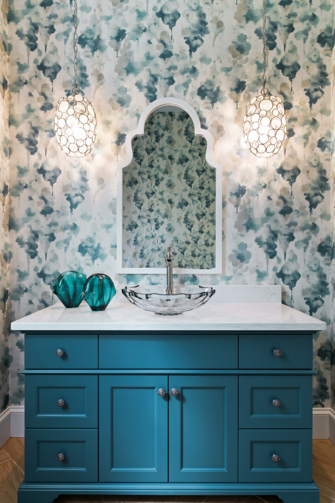 Design ideas for a mid-sized beach style powder room in Tampa with recessed-panel cabinets, turquoise cabinets, a two-piece toilet, multi-coloured walls, porcelain floors, a vessel sink, engineered quartz benchtops, brown floor, white benchtops, a freestanding vanity and wallpaper.