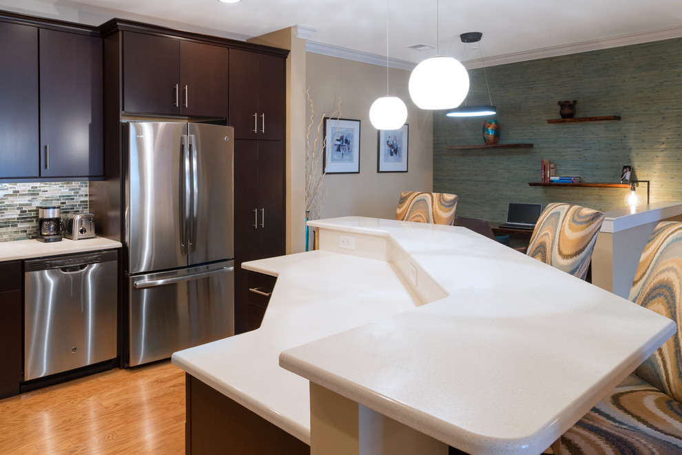 Inspiration for a mid-sized contemporary l-shaped eat-in kitchen in Philadelphia with an undermount sink, flat-panel cabinets, dark wood cabinets, quartz benchtops, blue splashback, glass sheet splashback, stainless steel appliances, light hardwood floors and with island.