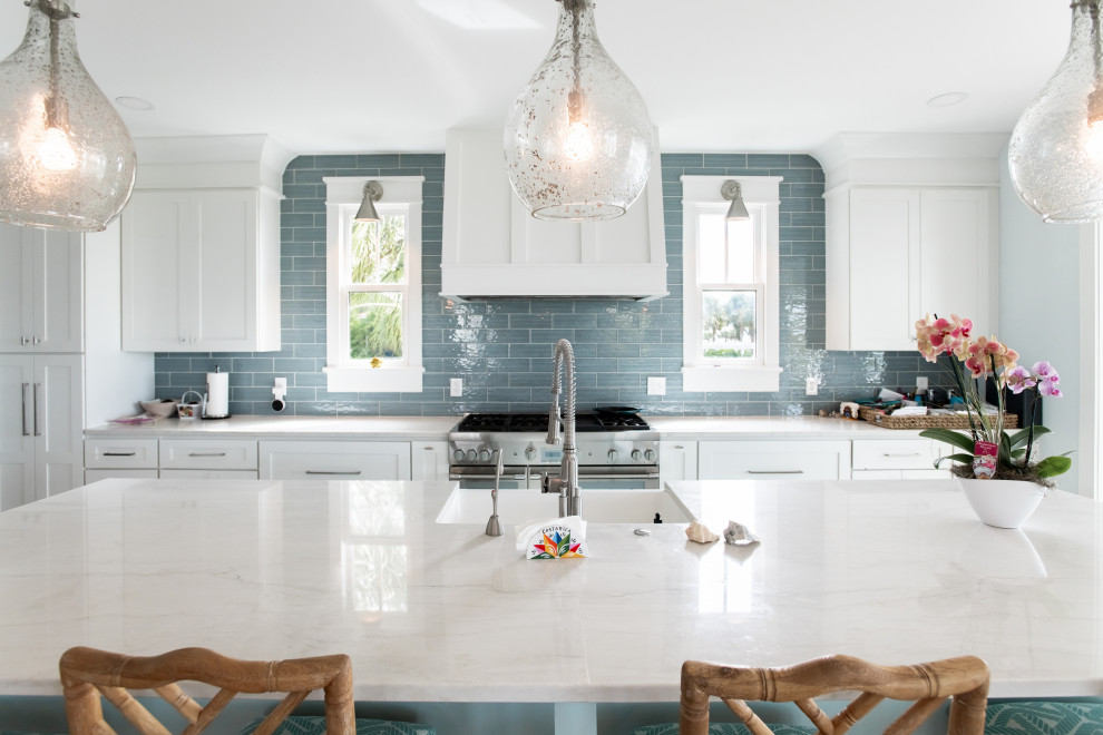 Photo of a large beach style single-wall eat-in kitchen in Charleston with a farmhouse sink, shaker cabinets, white cabinets, blue splashback, stainless steel appliances, medium hardwood floors, with island and white benchtop.